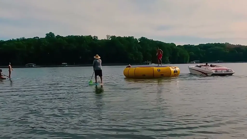 Guests paddleboarding past a water trampoline on the lake